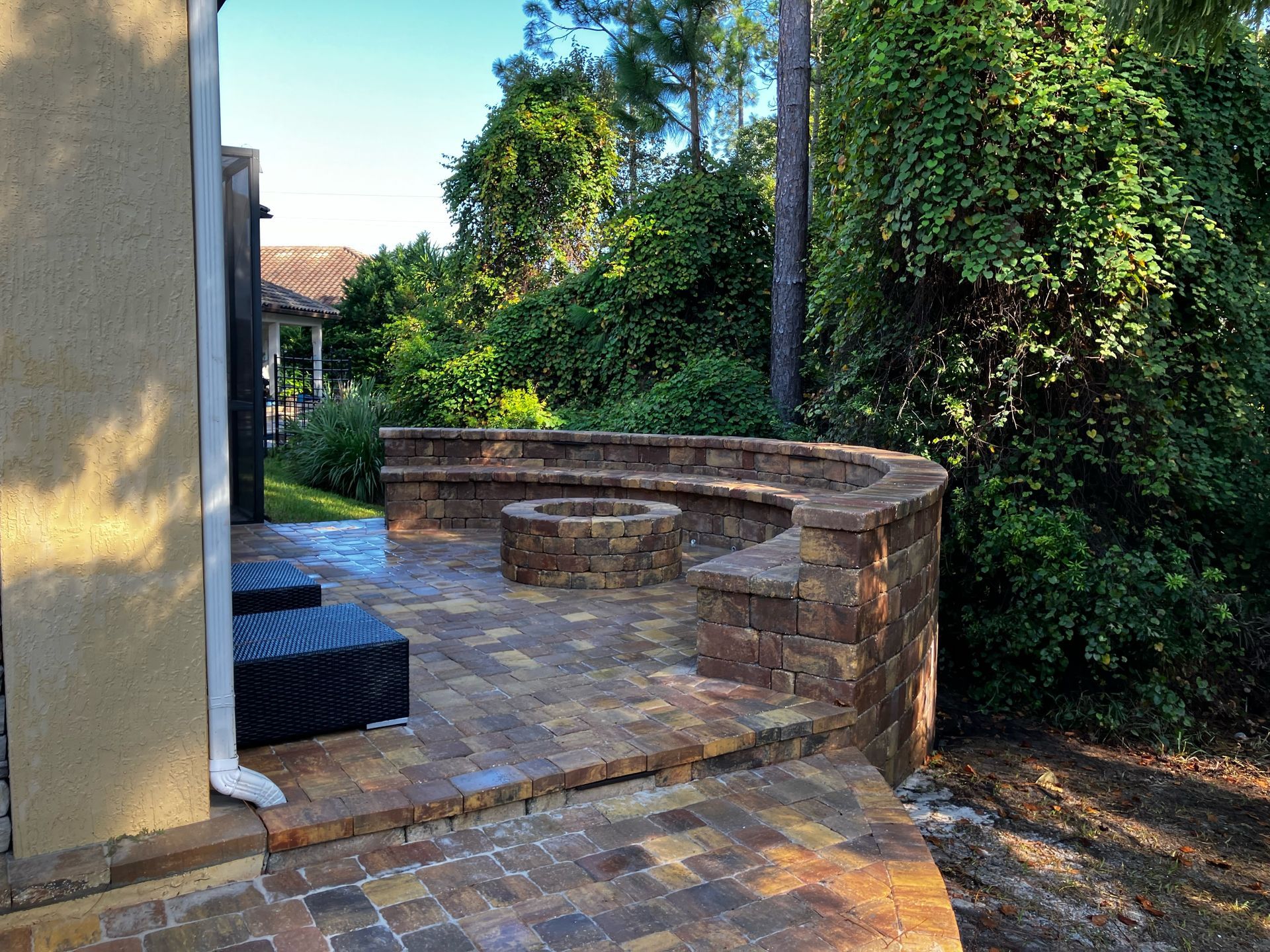 A paver patio with a fire pit in the middle of it and a retaining wall around it