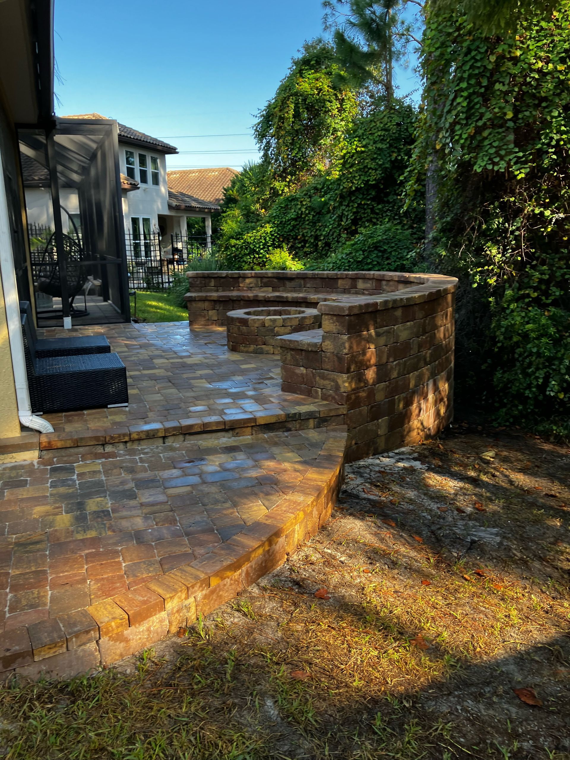 A red and orange paver patio with a fire pit in the backyard of a house.