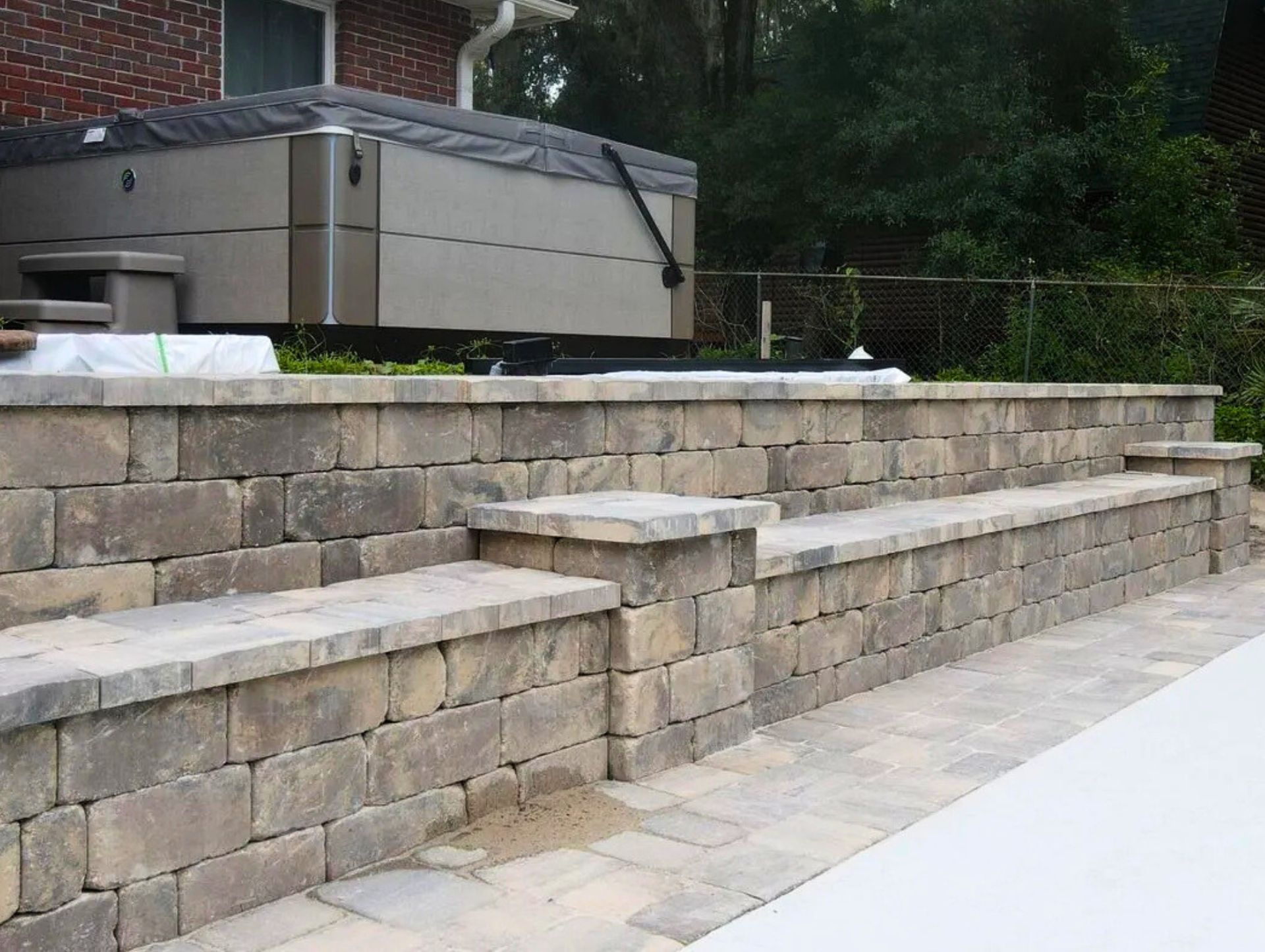Stone retaining wall with built-in bench seating and steps leading to a raised hot tub beside a brick house.