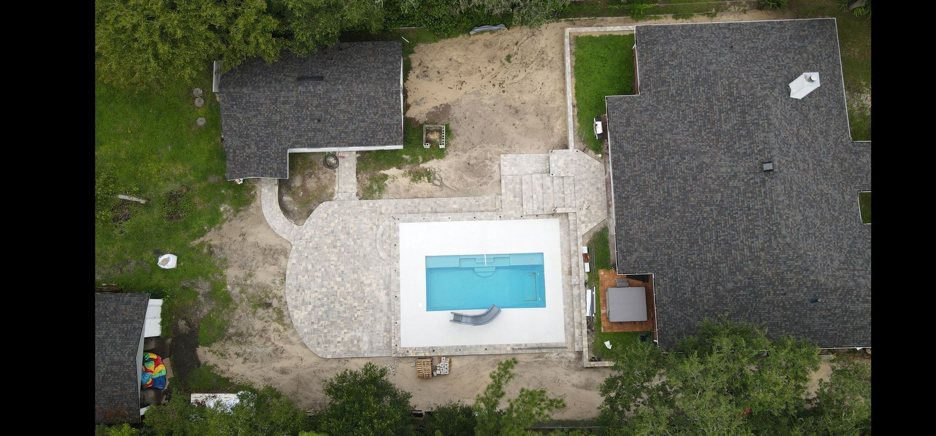 An aerial view of a house with a swimming pool in the backyard and a new paver patio and pool deck.