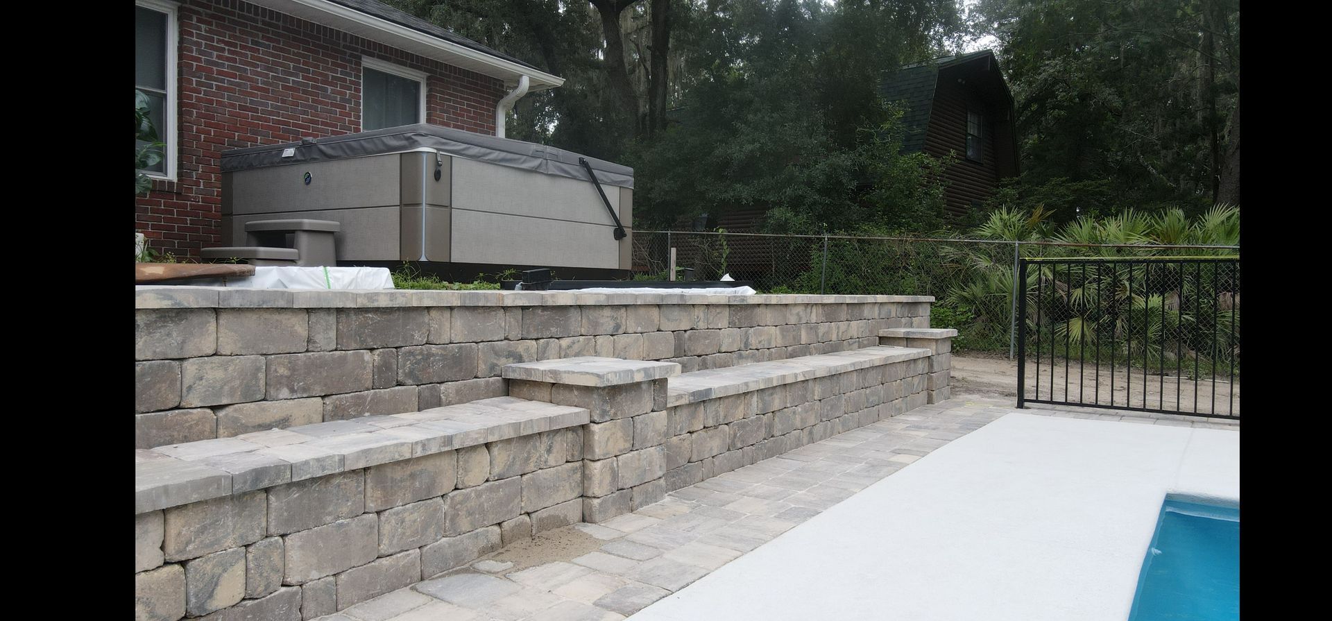 A hot tub is sitting on top of a stone wall next to a swimming pool.