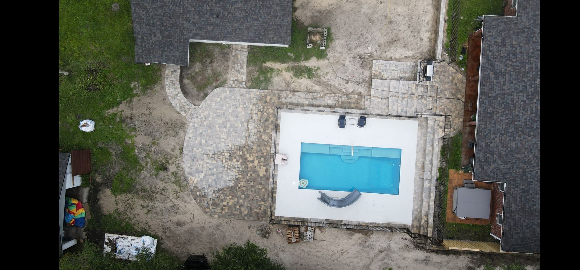 An aerial view of a swimming pool in the backyard of a house with a newly installed paver patio