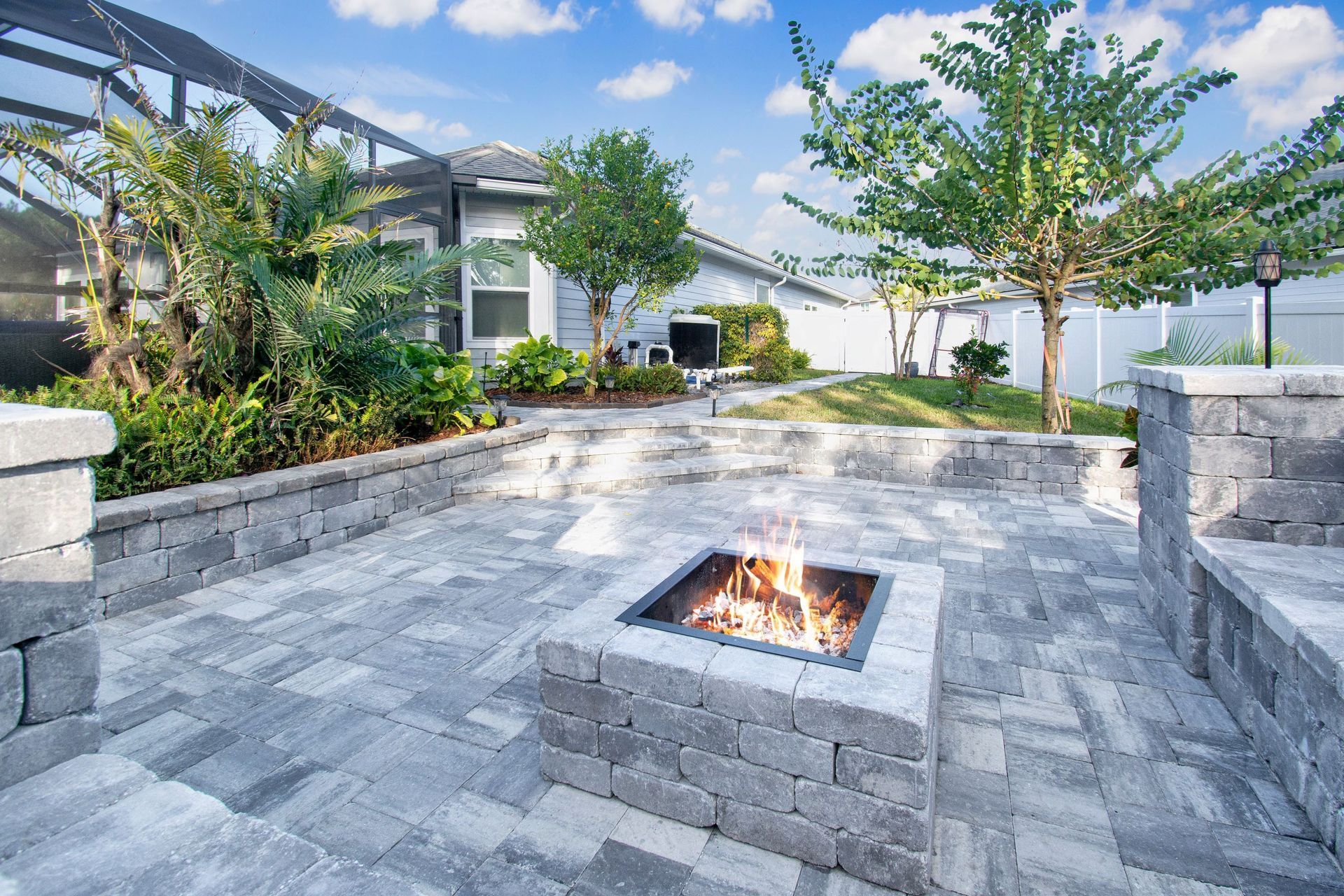 There is a fire pit with a fire in the middle of the paver patio.