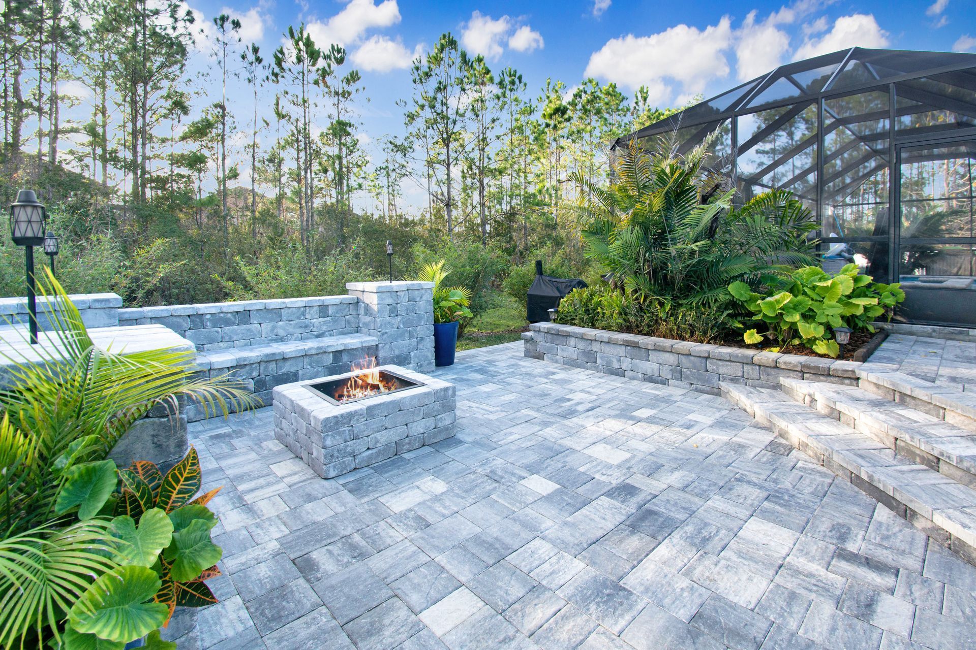 There is a fire pit in the middle of a large grey paver patio.