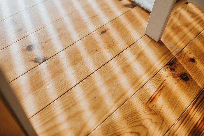 A close up of a wooden floor with the sun shining through the blinds.