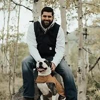 A man is sitting on a rock with a dog on his back.