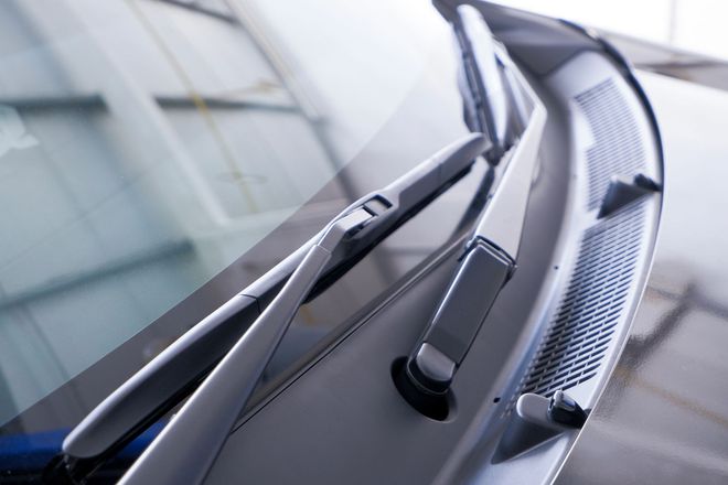 Vista ravvicinata dei tergicristalli e della griglia di protezione in plastica nera di un'auto.