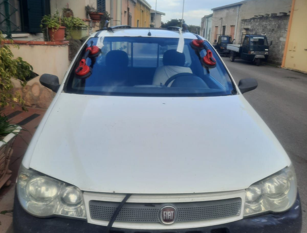 Una Fiat bianca parcheggiata in una strada stretta, con due ventose rosse attaccate alla parte superiore del parabrezza.