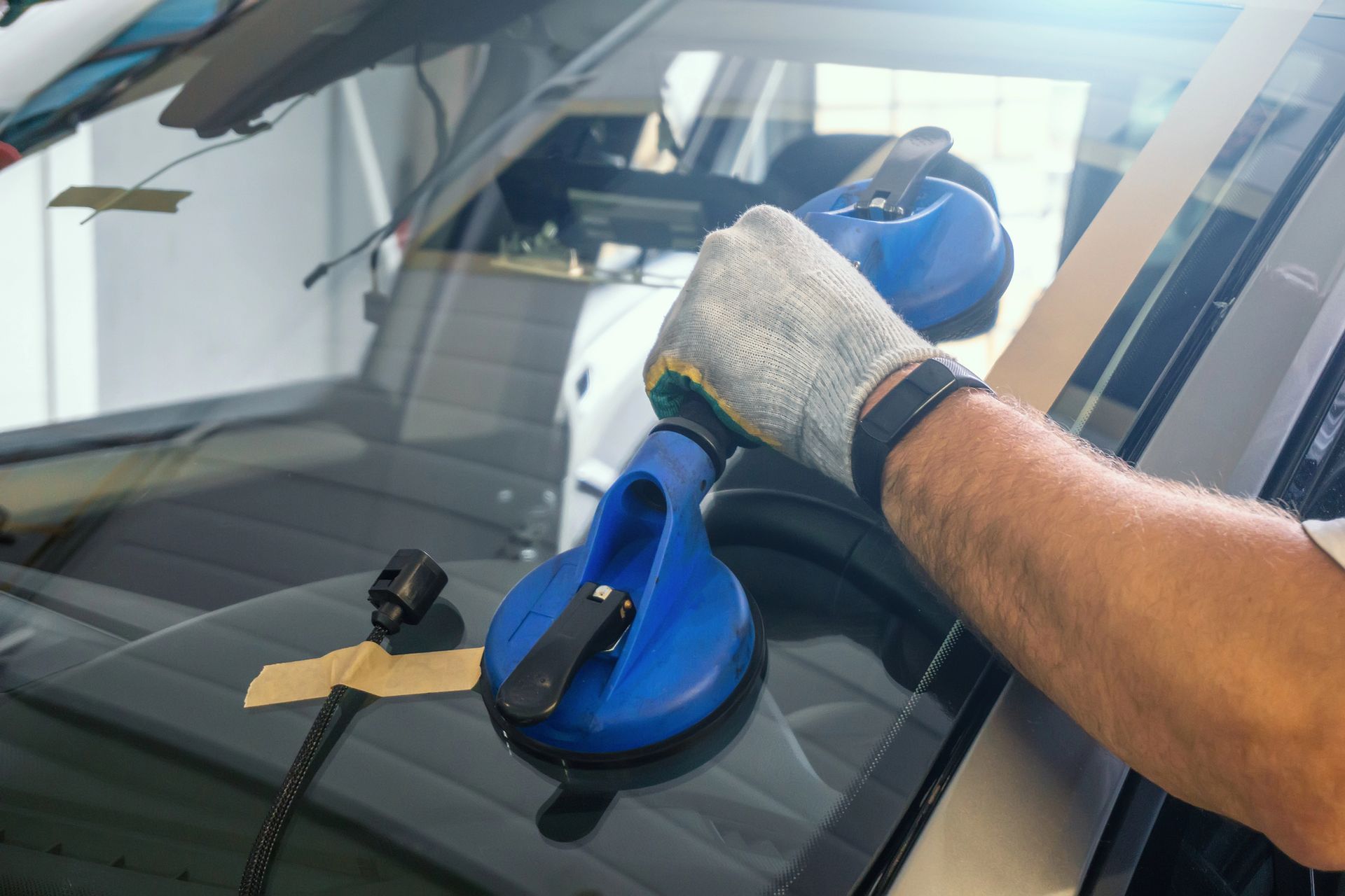 Una mano guantata utilizza una ventosa blu per installare o rimuovere il parabrezza di un'auto.