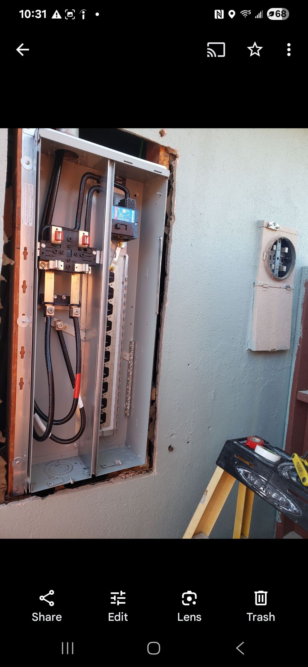 A picture of an electrical box on a wall with a ladder next to it.