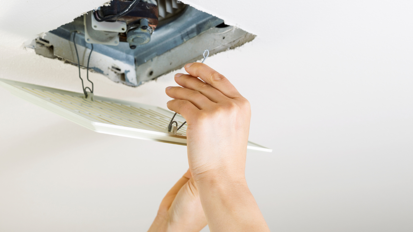 Hands installing a bathroom vent cover into a ceiling.
