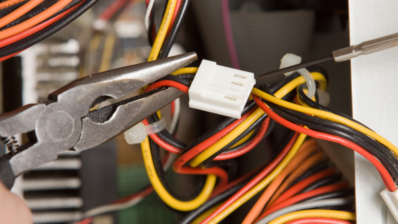 Close-up of a person using pliers and screwdriver on a computer's colorful wires and connectors.