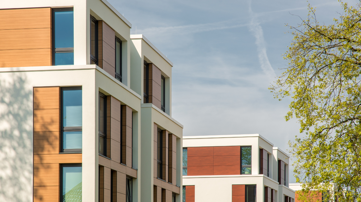 Modern white apartment buildings with wooden and brown accents; blue sky.