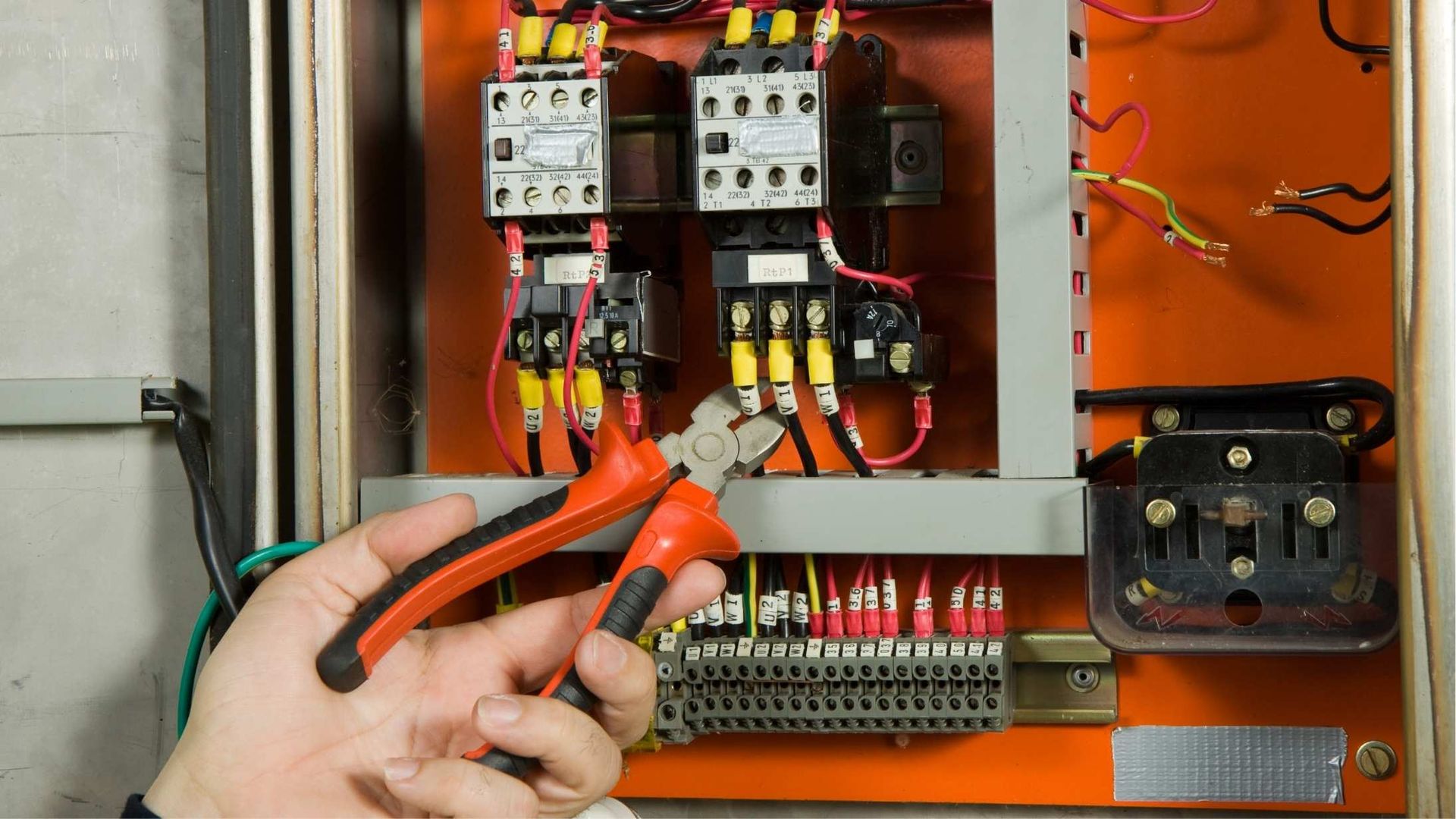 A person is working on an electrical box with a pair of pliers.
