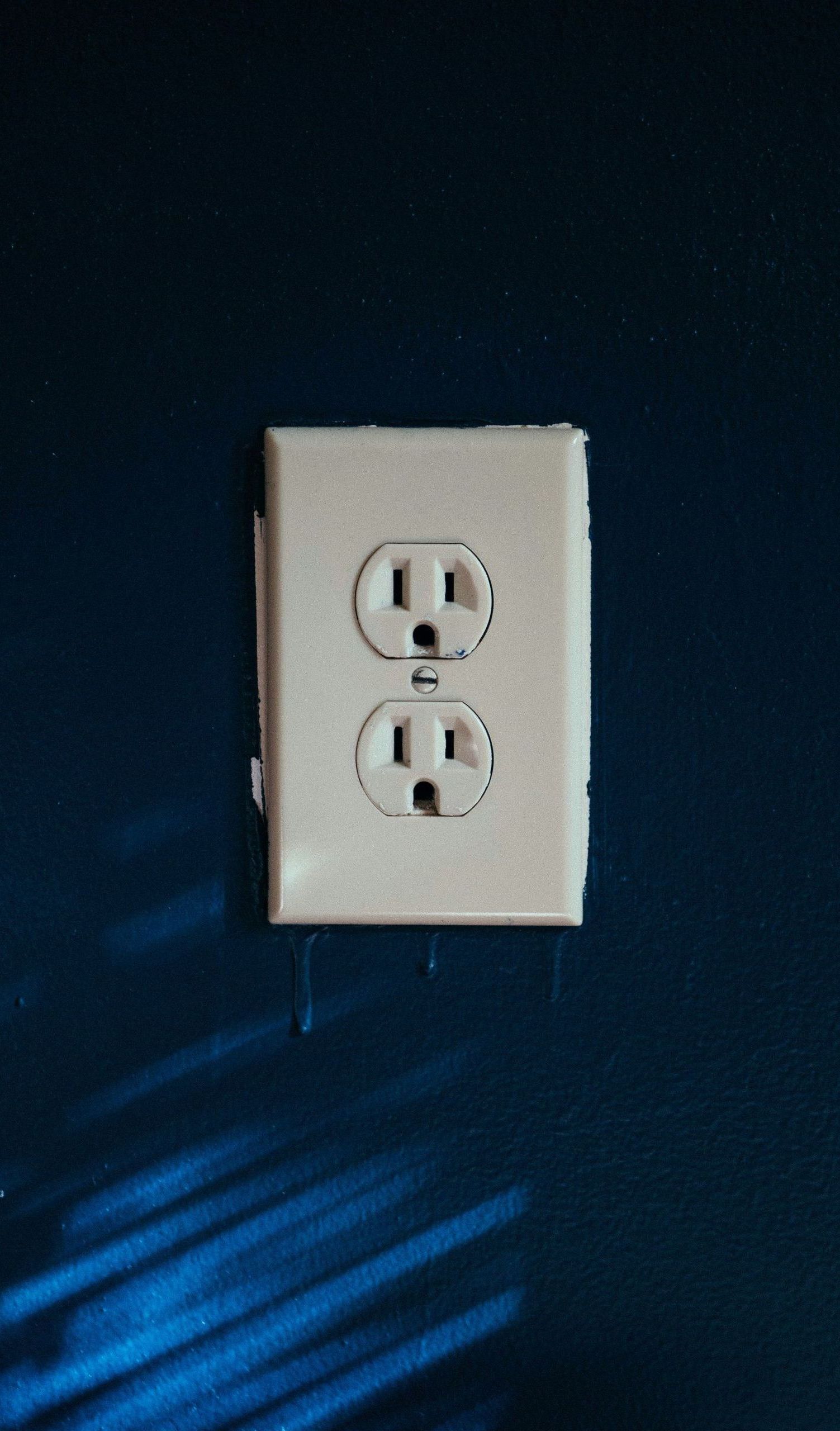 Beige electrical outlet on a dark blue wall.