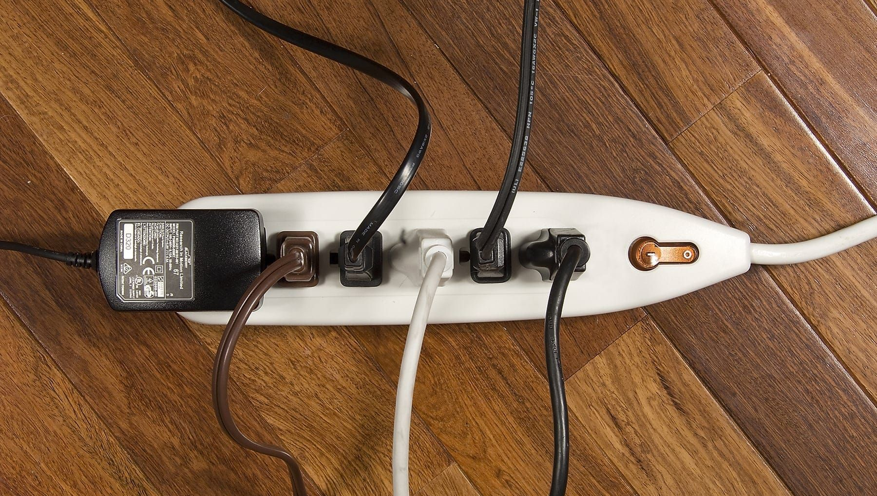 Power strip on hardwood floor with several cords plugged in.