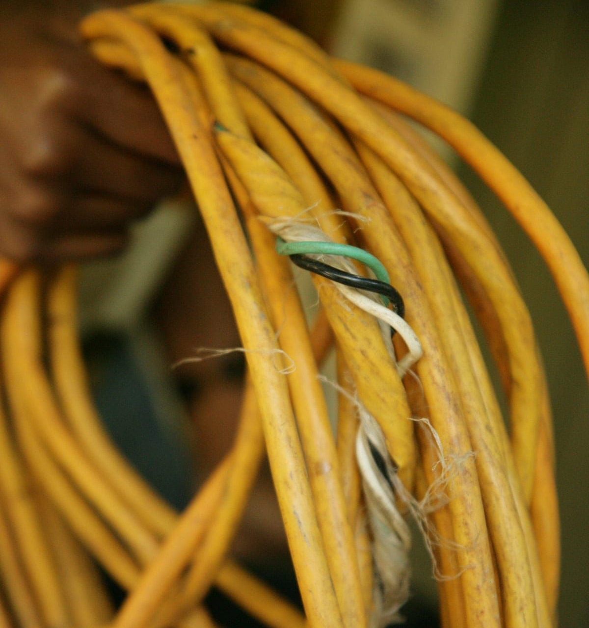Damaged yellow extension cord with exposed wires: black, white, and green.