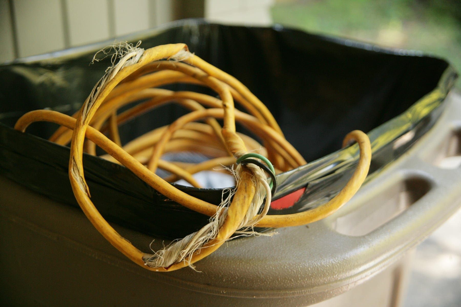 Tangled yellow electrical cord in a black trash can, frayed at one end.