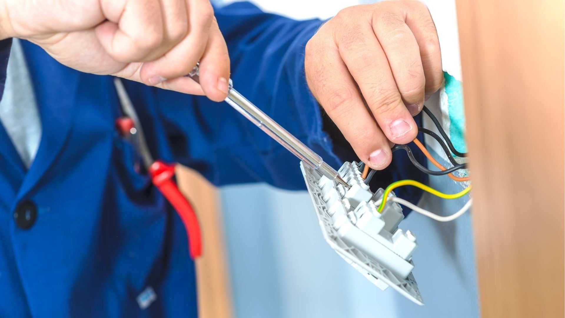 An electrician is fixing a light switch with a screwdriver.