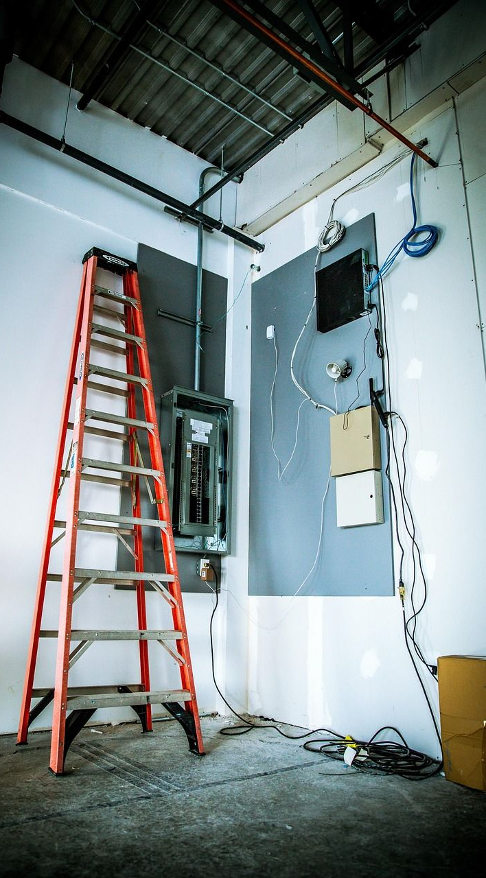 Red ladder next to electrical panel in unfinished room; cables and wires are visible.