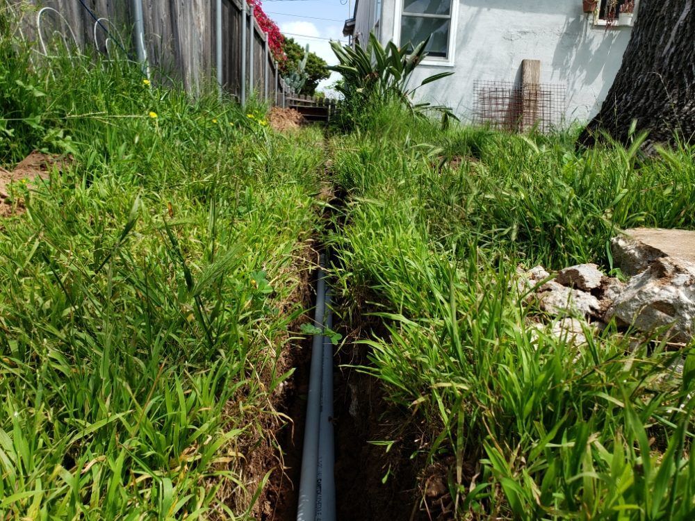 A drain pipe is being installed in the grass next to a house.