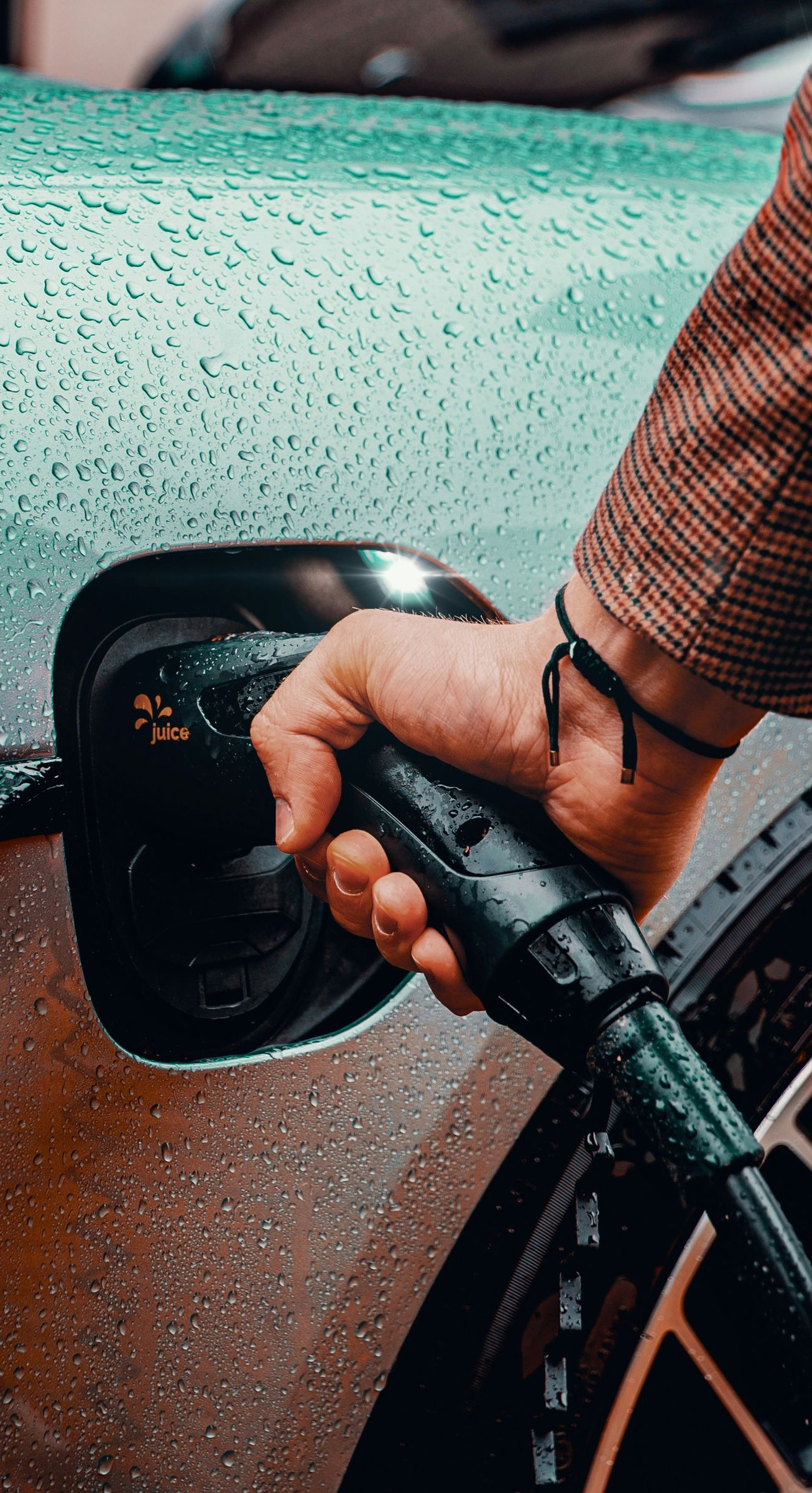 Person plugging in an electric car with a charging cable. Wet car with rain drops.