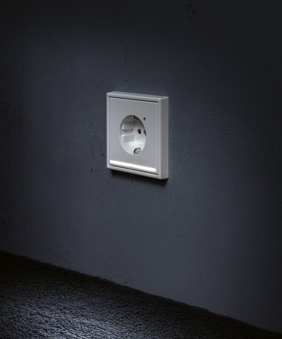 A white electrical outlet on a dark gray wall, with a glowing light strip below.