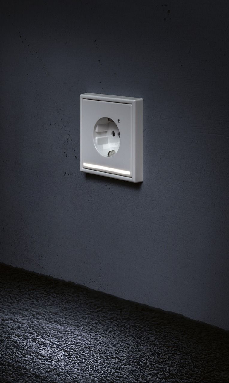 A white electrical outlet on a dark gray wall, with a glowing light strip below.