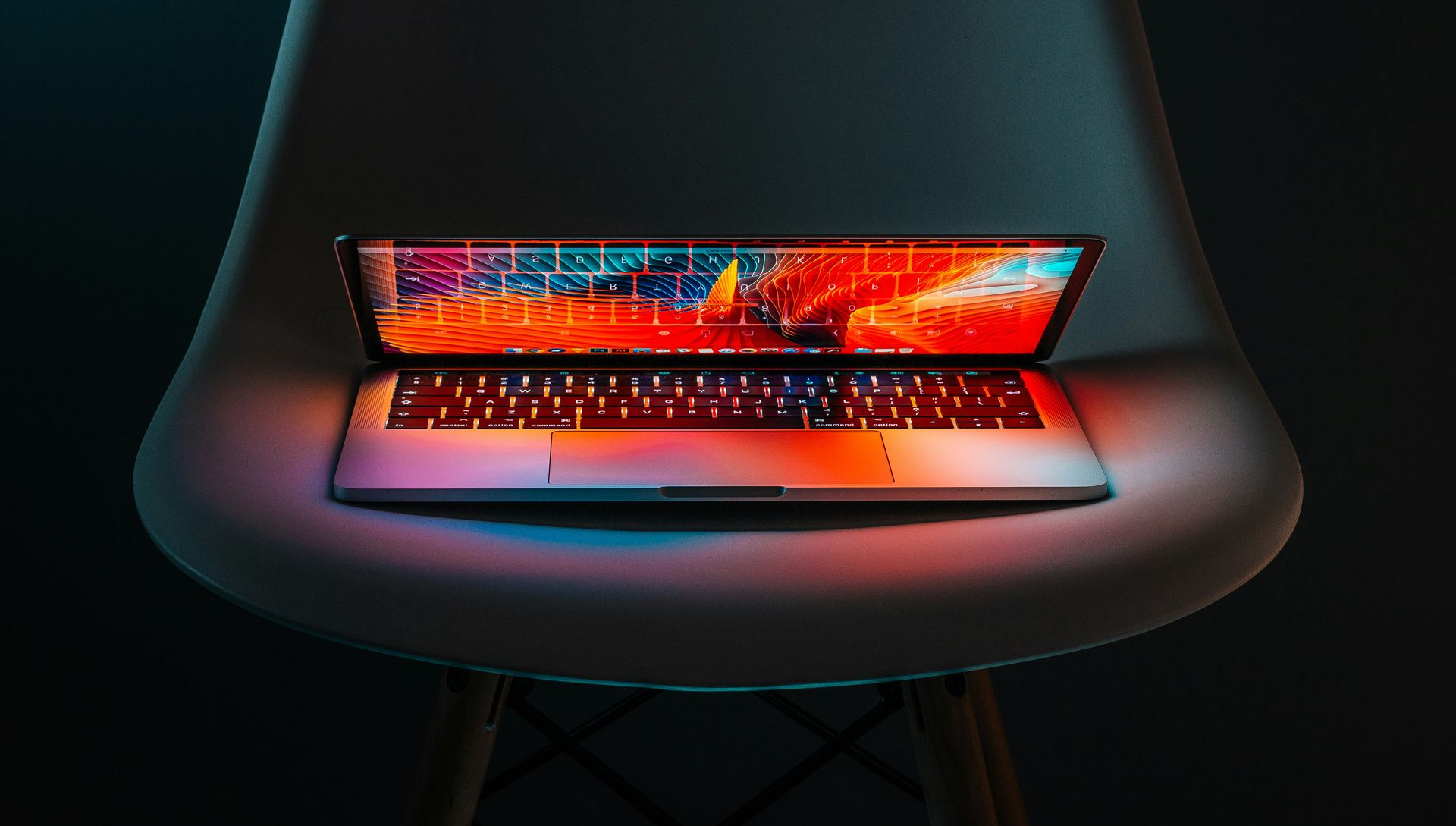 Laptop on a chair, lit with vibrant colors of red, orange, and blue against a dark background.