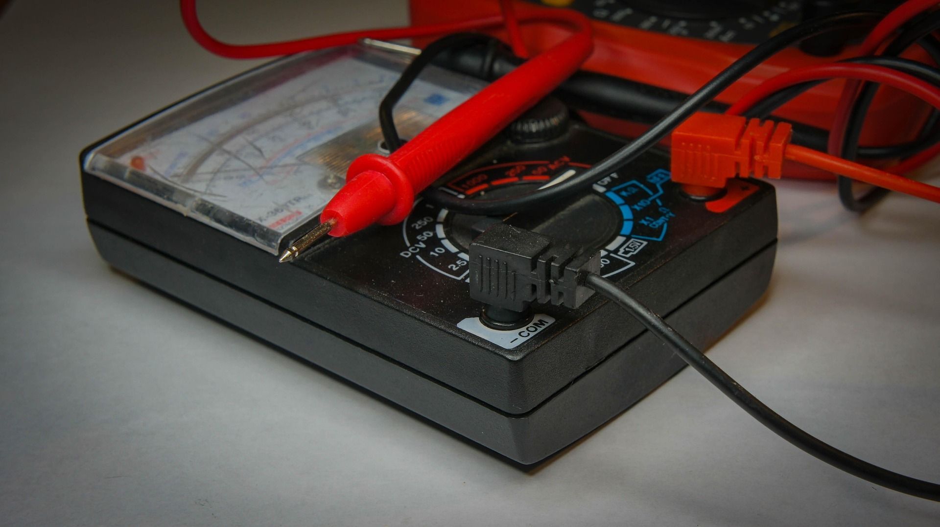 Black and red multimeter with probes and dial for measuring electrical values.