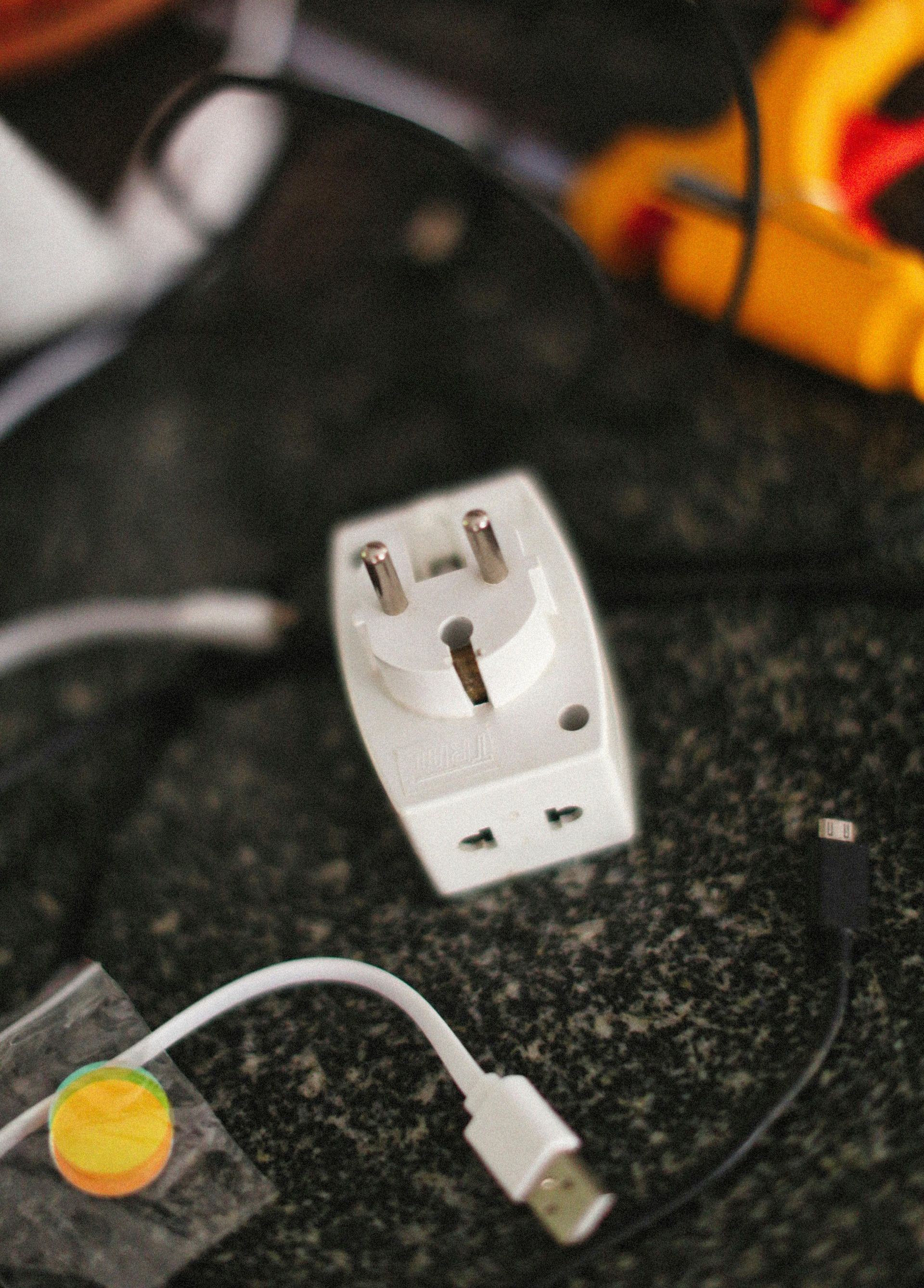 White power adapter with EU plug, near USB cables, on a dark, speckled surface.