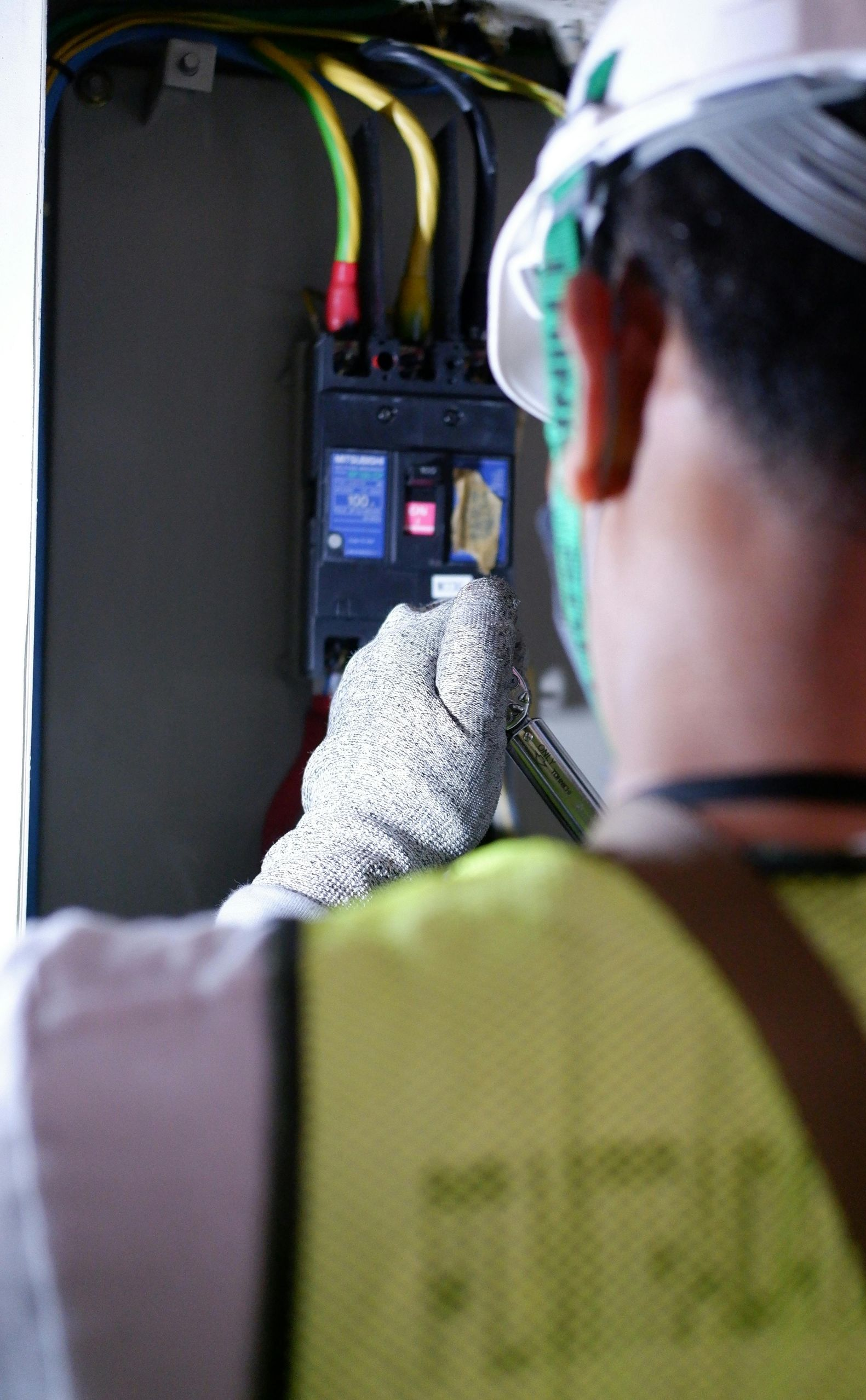Electrician in safety gear, manipulating a circuit breaker in an electrical panel.