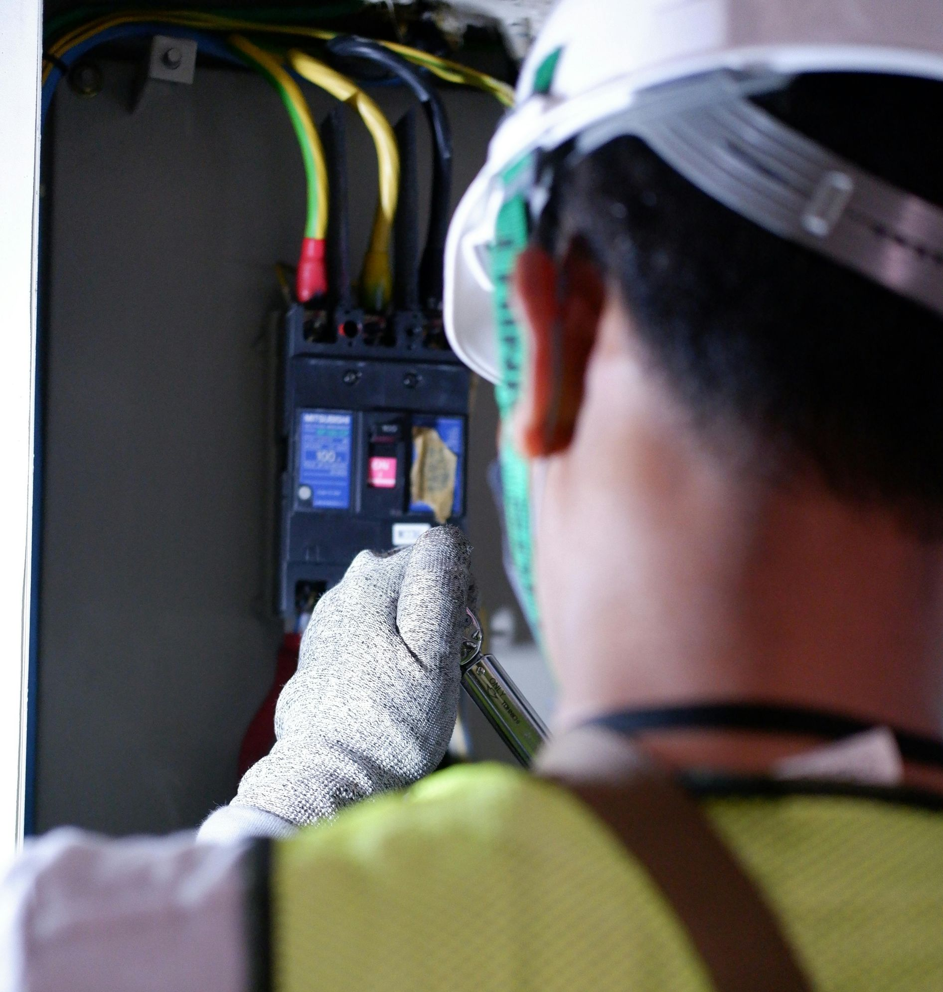 Electrician working on a circuit breaker, wearing gloves, a hard hat, and a safety vest.