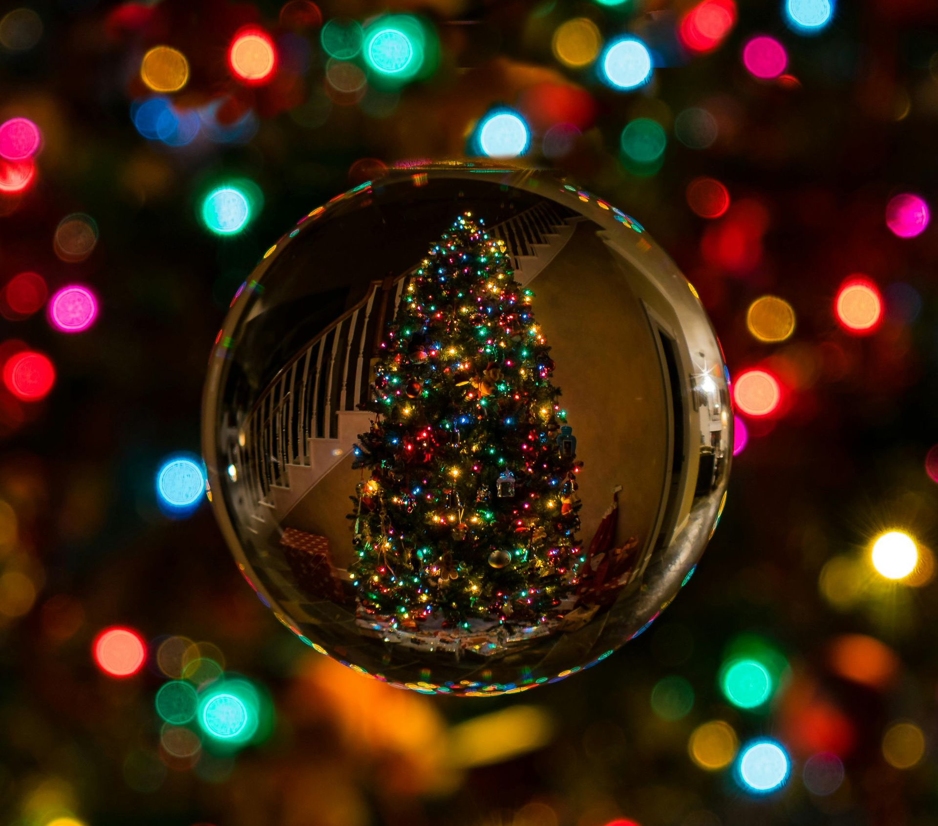Christmas tree reflected in a clear glass ball, with colorful lights out of focus in the background.