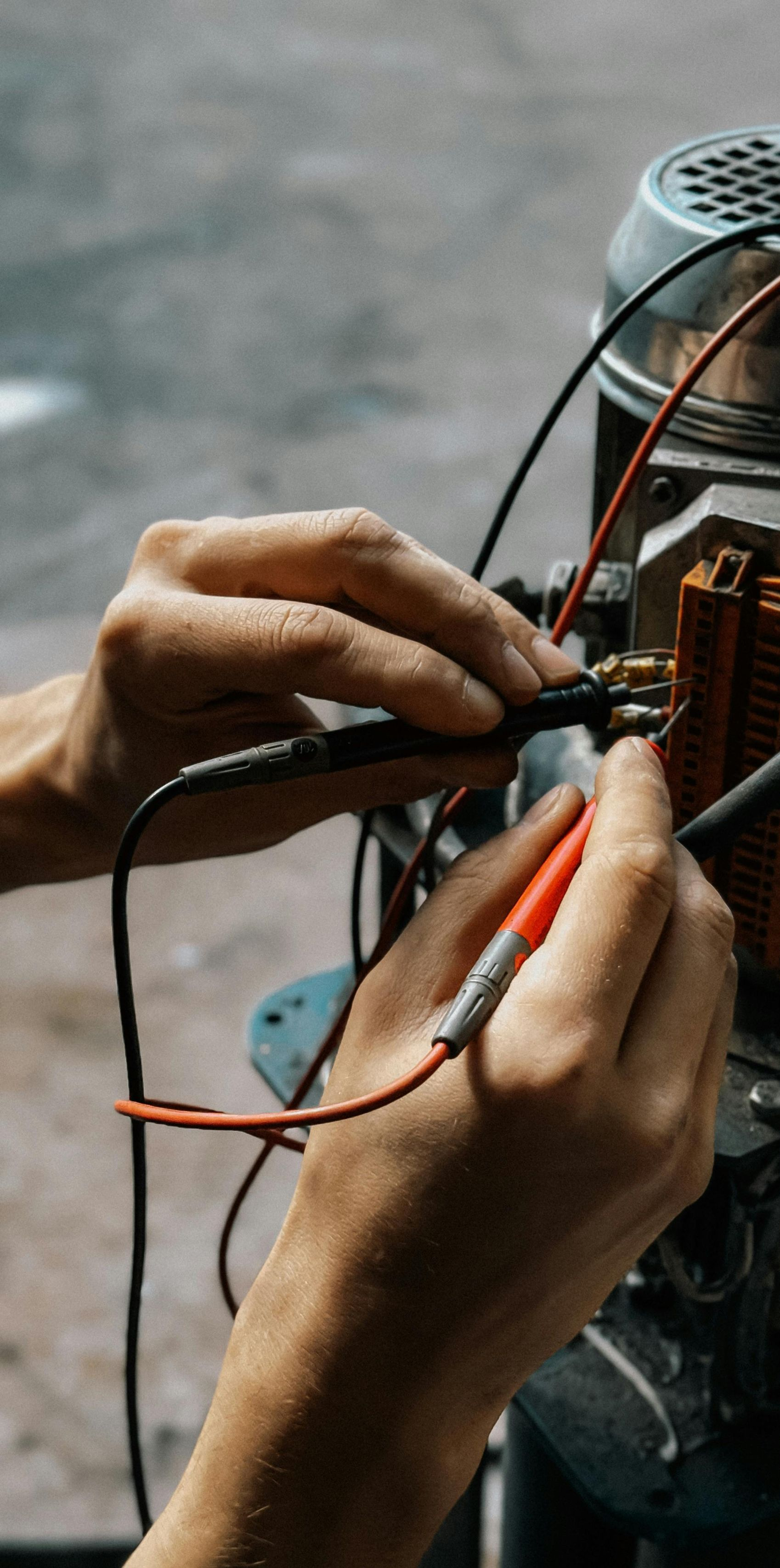 Hands using electrical testing probes on machinery. Red and black wires are visible.
