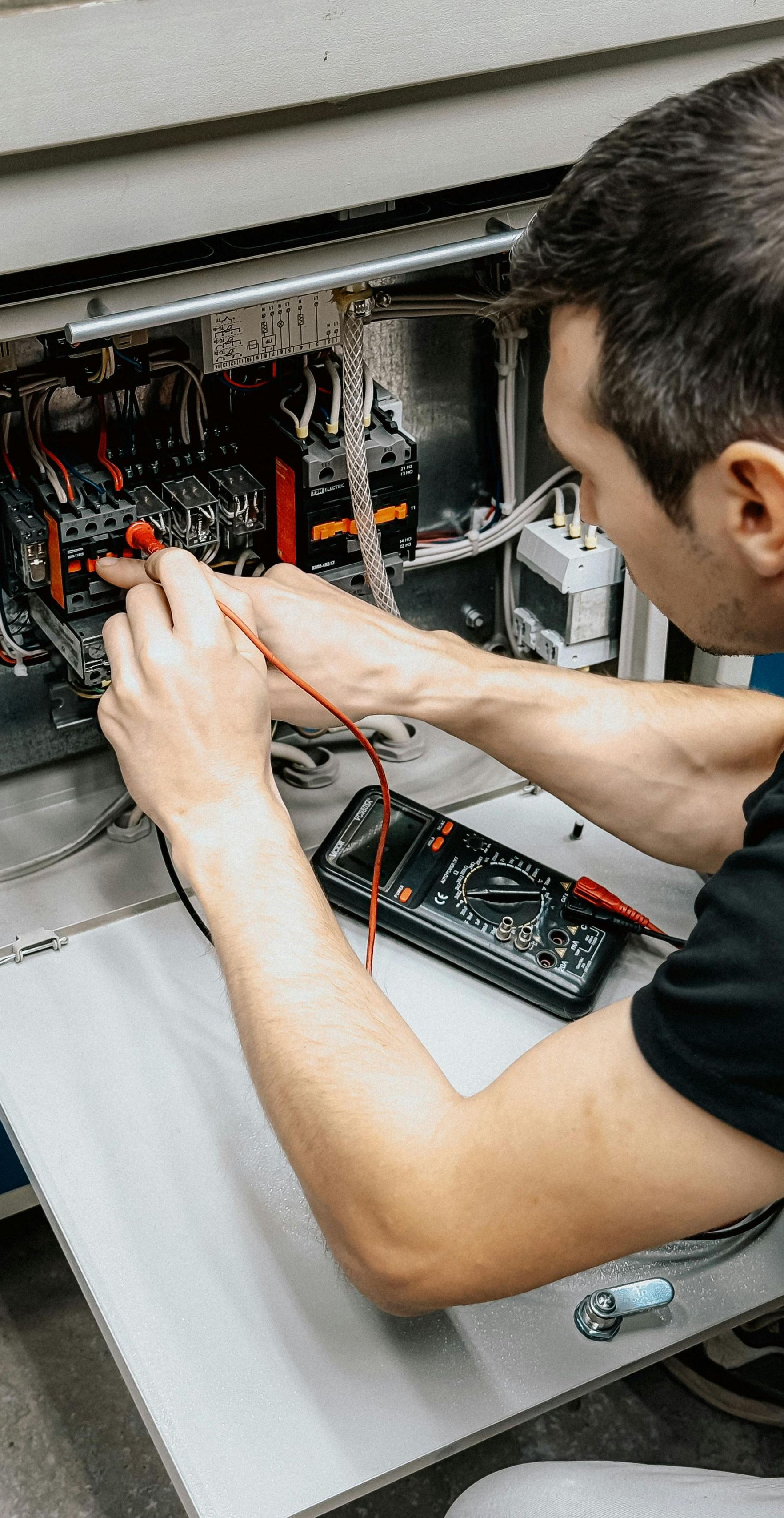 Man using multimeter to test electrical components inside a machine.