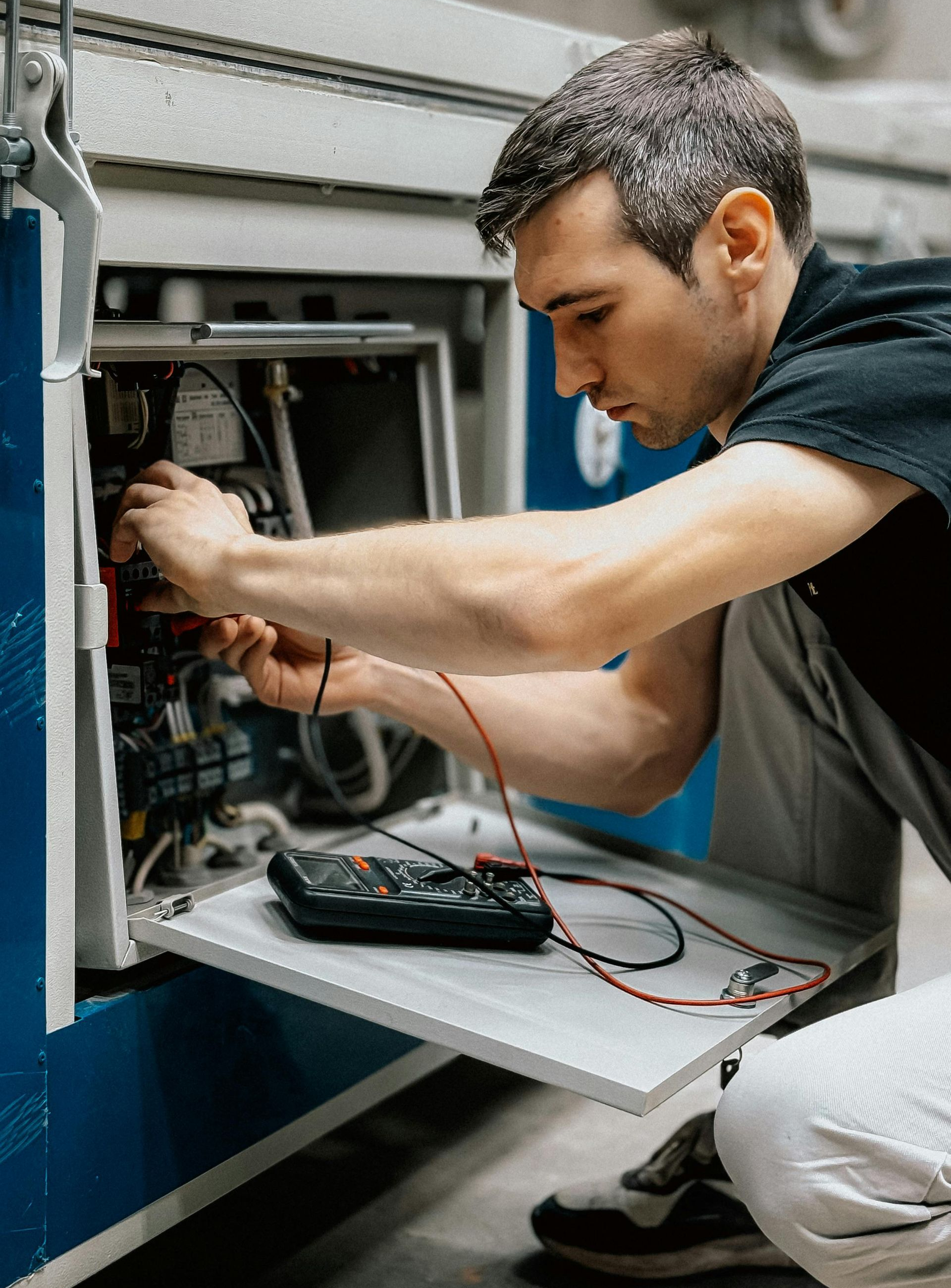 Man using a multimeter to inspect electrical components inside machinery.