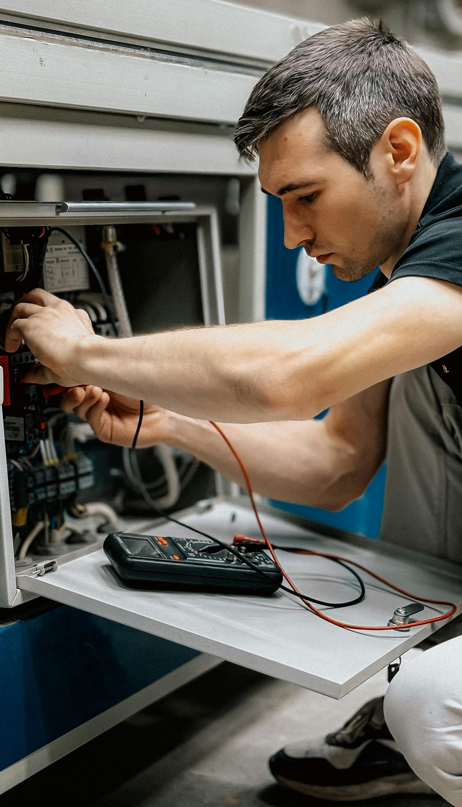 Man working on machinery, using a multimeter; interior setting.
