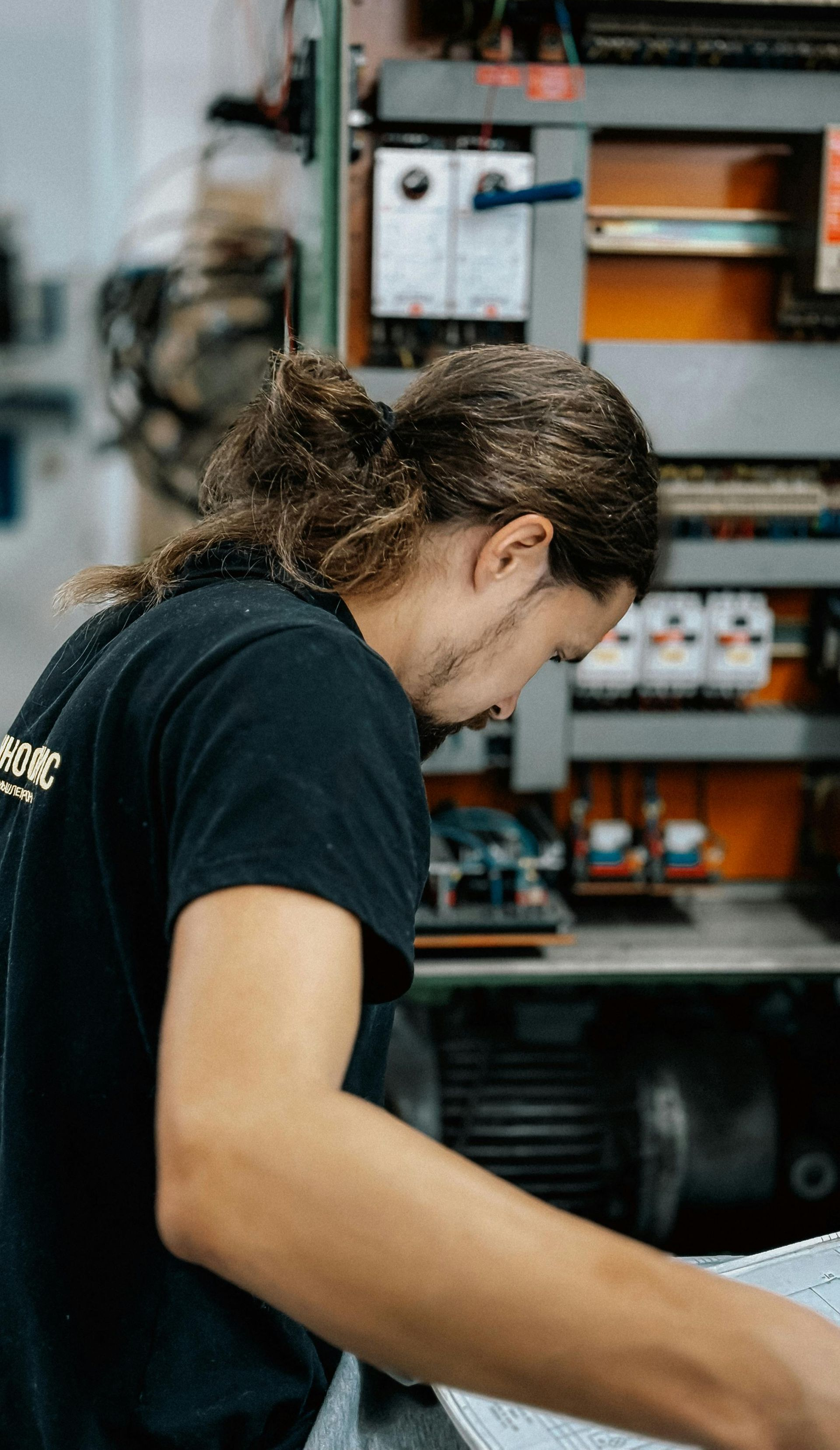 Man with long hair working on machinery, in industrial setting.