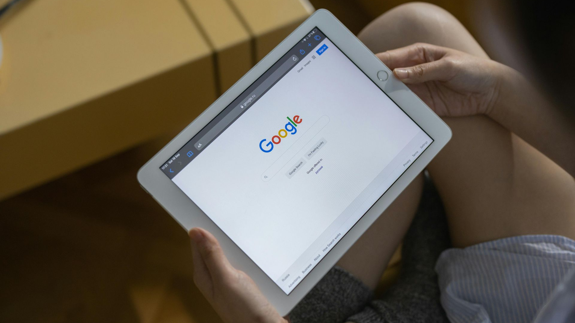 A person sitting and holding a tablet displaying the Google homepage.