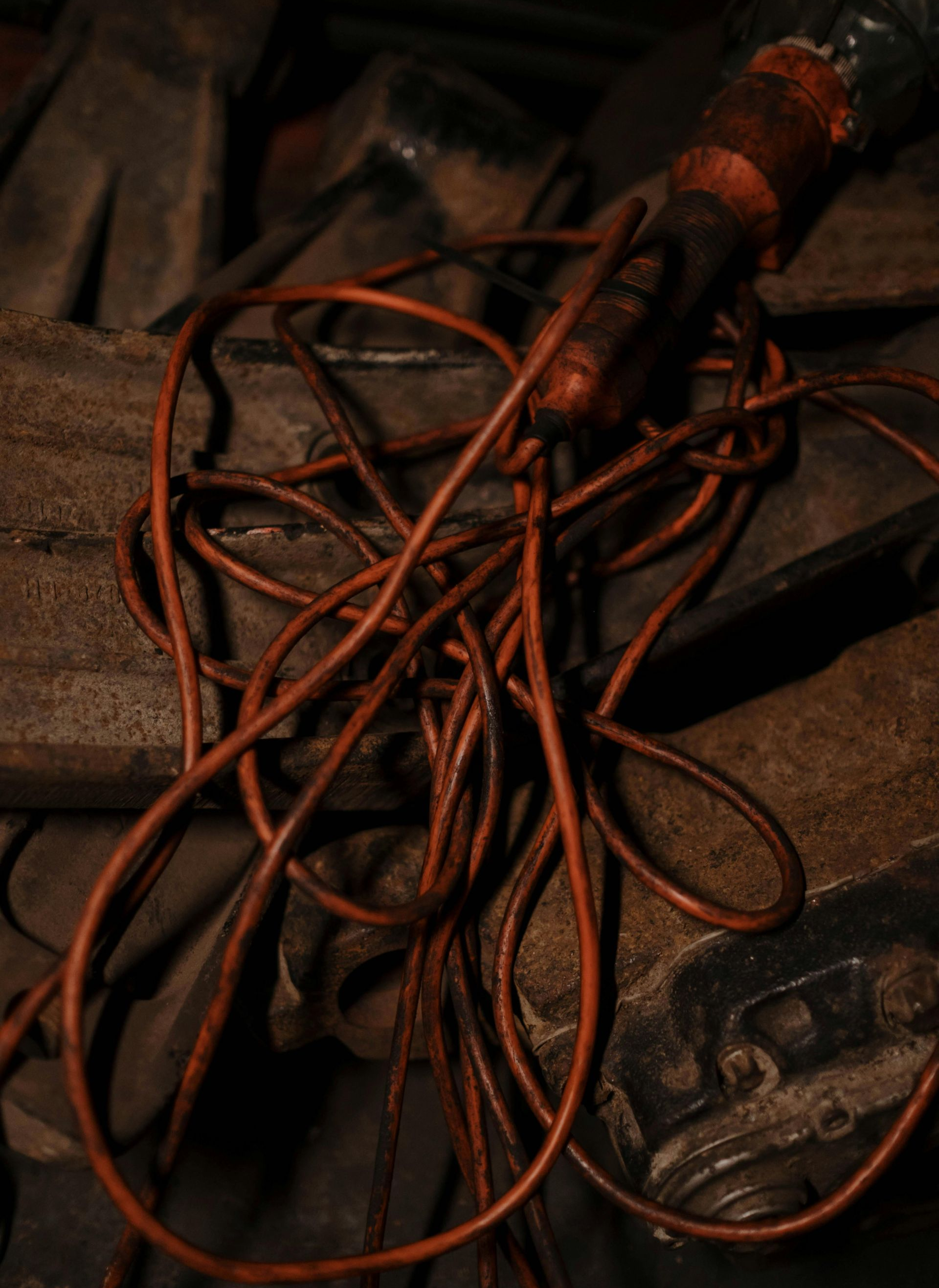 Tangled orange extension cord atop a dark, rough surface in a dimly lit setting.
