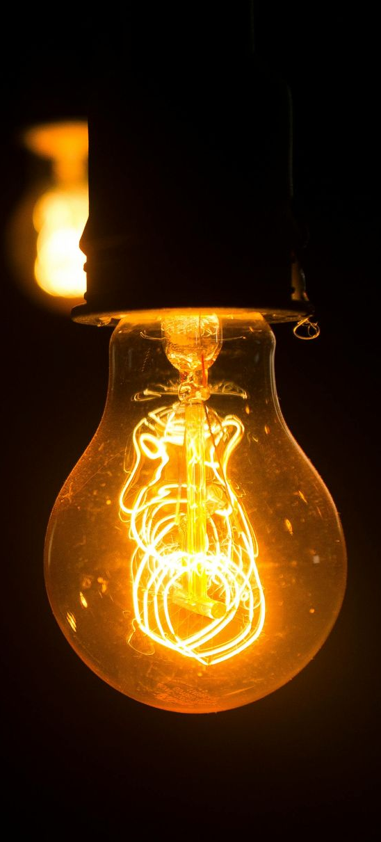 Glowing Edison lightbulb against a dark background; orange filaments shine.
