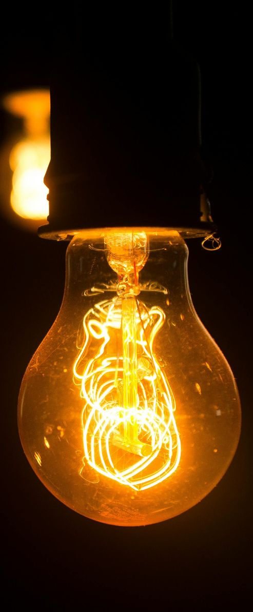 Glowing Edison lightbulb against a dark background; orange filaments shine.