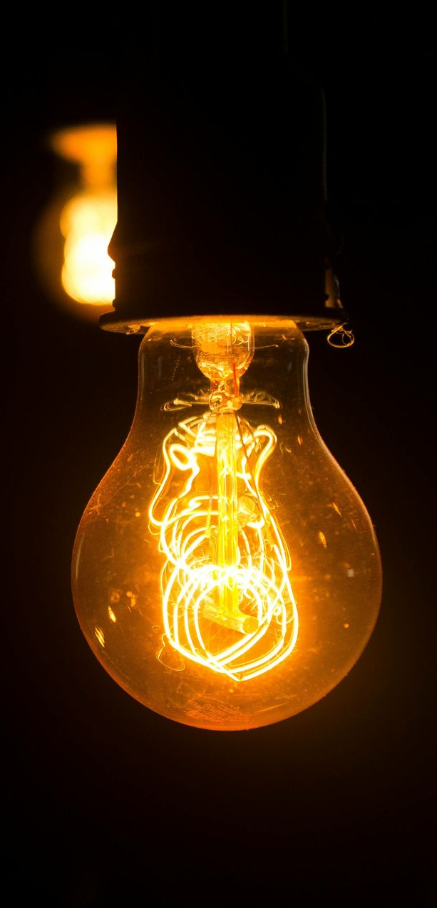 Glowing Edison lightbulb against a dark background; orange filaments shine.