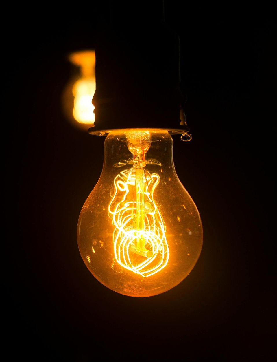 Glowing Edison lightbulb against a dark background; orange filaments shine.