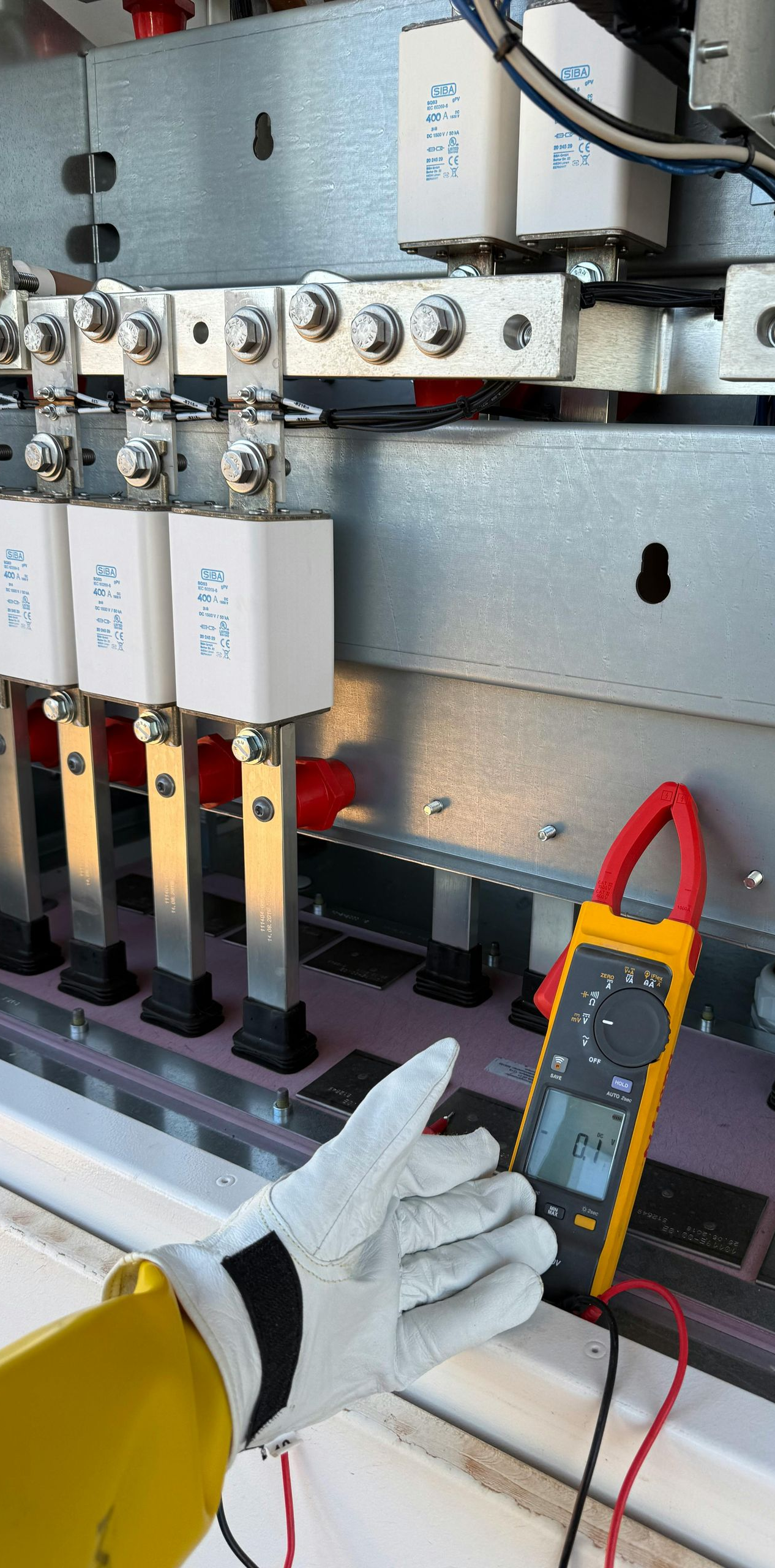 A gloved hand holds a multimeter near electrical components.