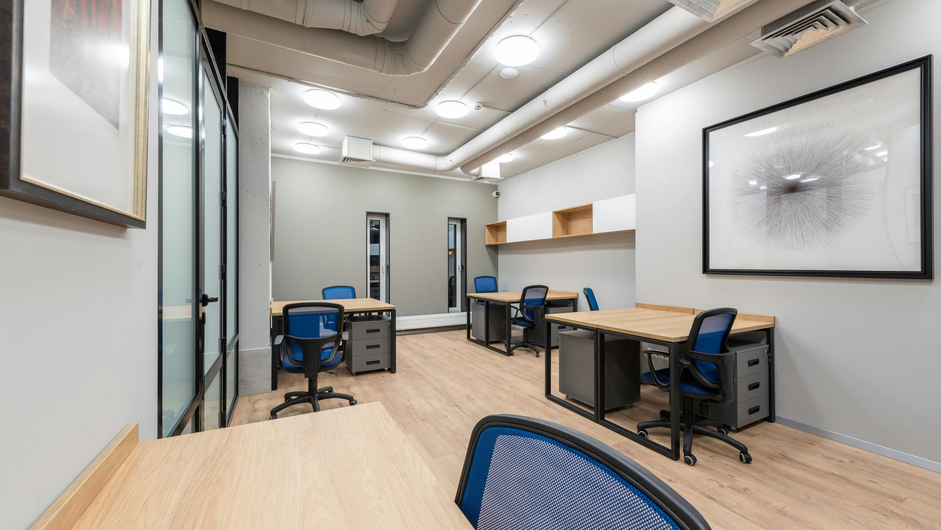 Office with several desks, blue chairs, and artwork on the walls.