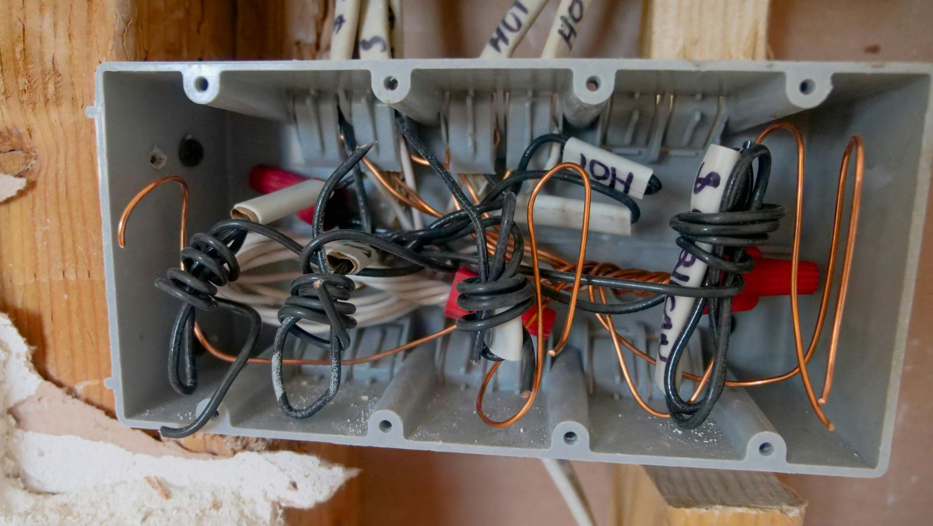 Gray electrical junction box with tangled wires and wire connectors.