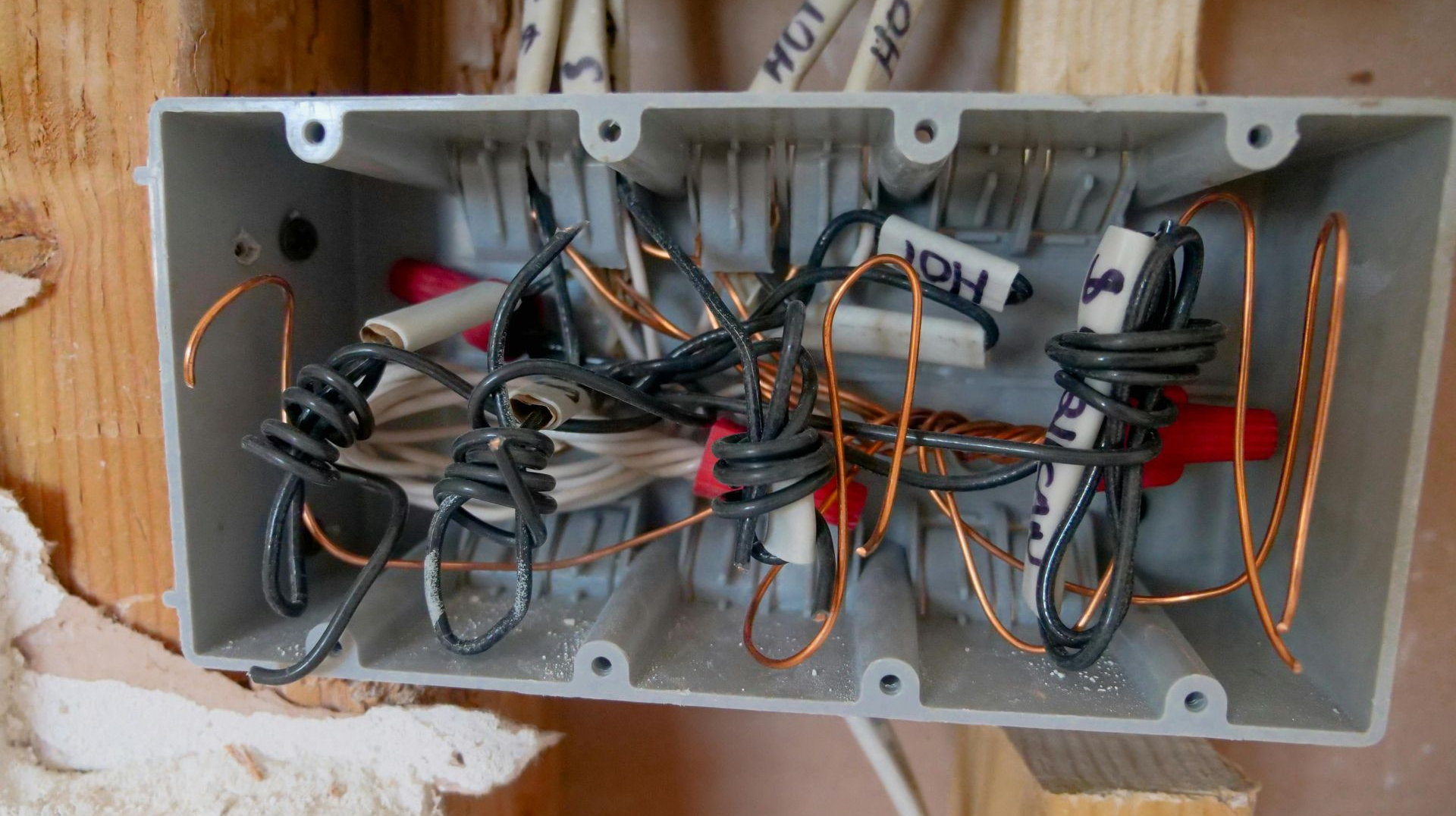 Electrical wires and connectors bundled inside a gray rectangular junction box mounted on wood.