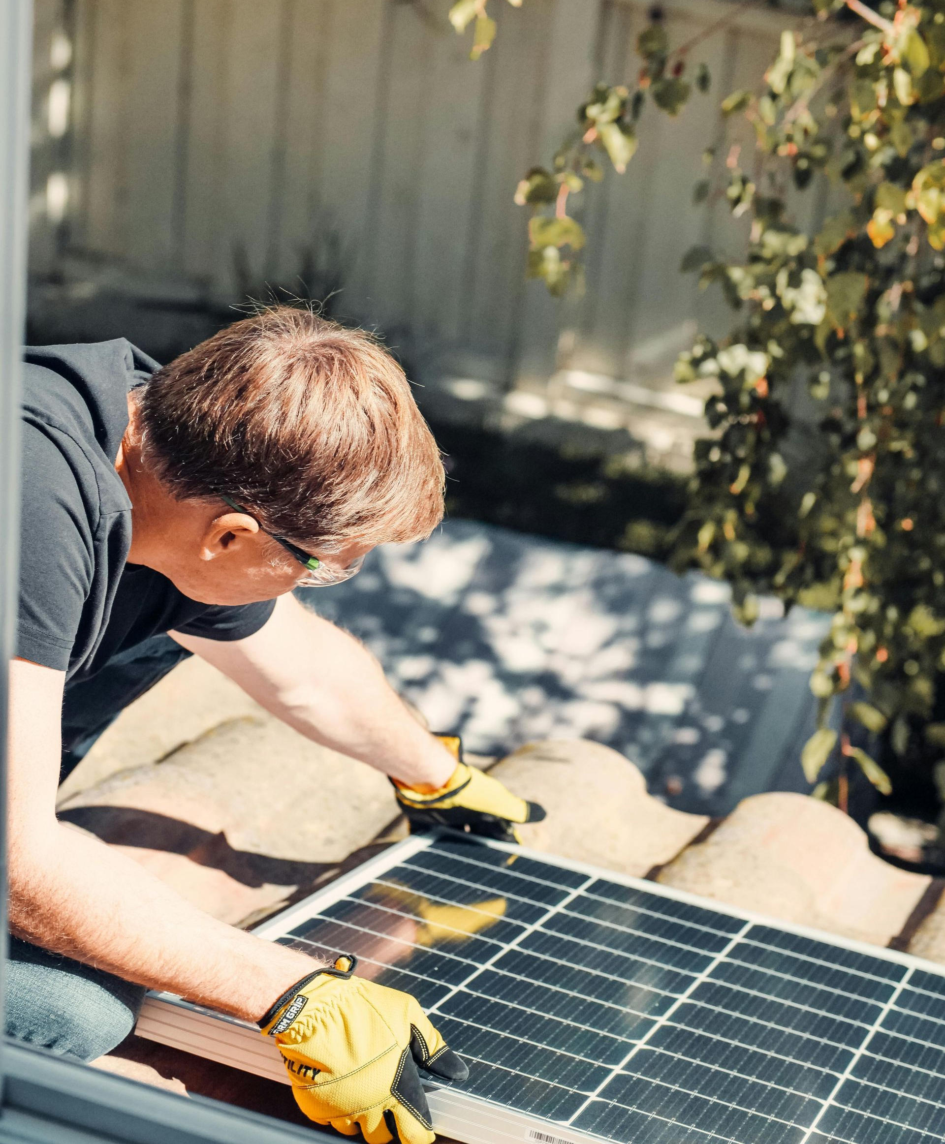 Man in gloves installing a solar panel on a rooftop, sunny day.
